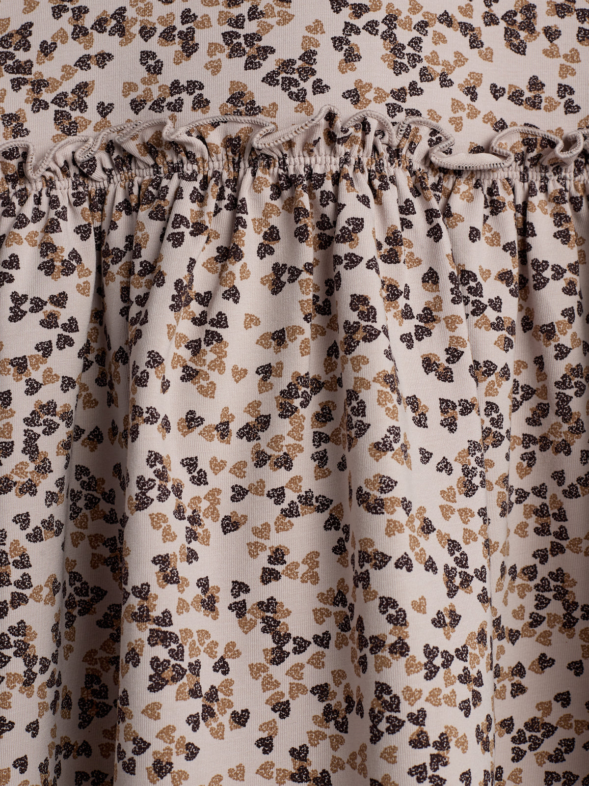 A patterned fabric features small, heart-like clusters in brown and beige. The fabric is gathered with elastic stitching, creating a ruffled texture, set against a neutral background.