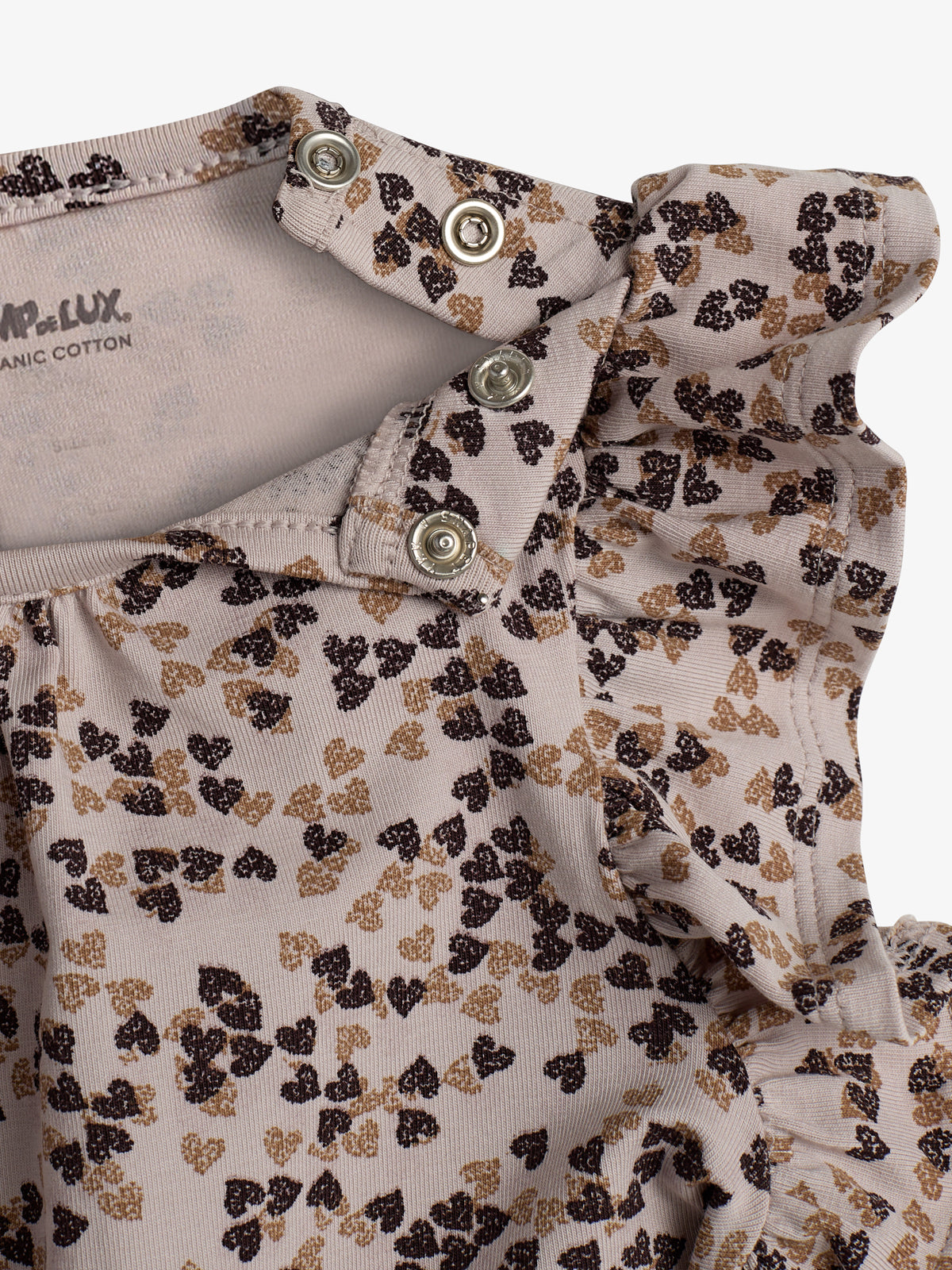 Shirt with ruffled collar and button snaps, featuring a pattern of small brown and black hearts. Text: "SMALL de LUX ORGANIC COTTON." Light background.