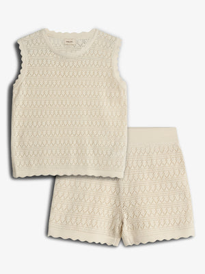 A cream-colored sleeveless knit top and shorts set lies against a plain background, showcasing a delicate diamond pattern and scalloped edges, exuding a soft and casual style.