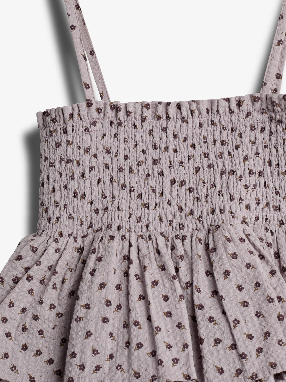 A fabric dress features a ruched bodice and skirt with thin shoulder straps, adorned with a pattern of small, dark floral prints on a light background, against a plain backdrop.