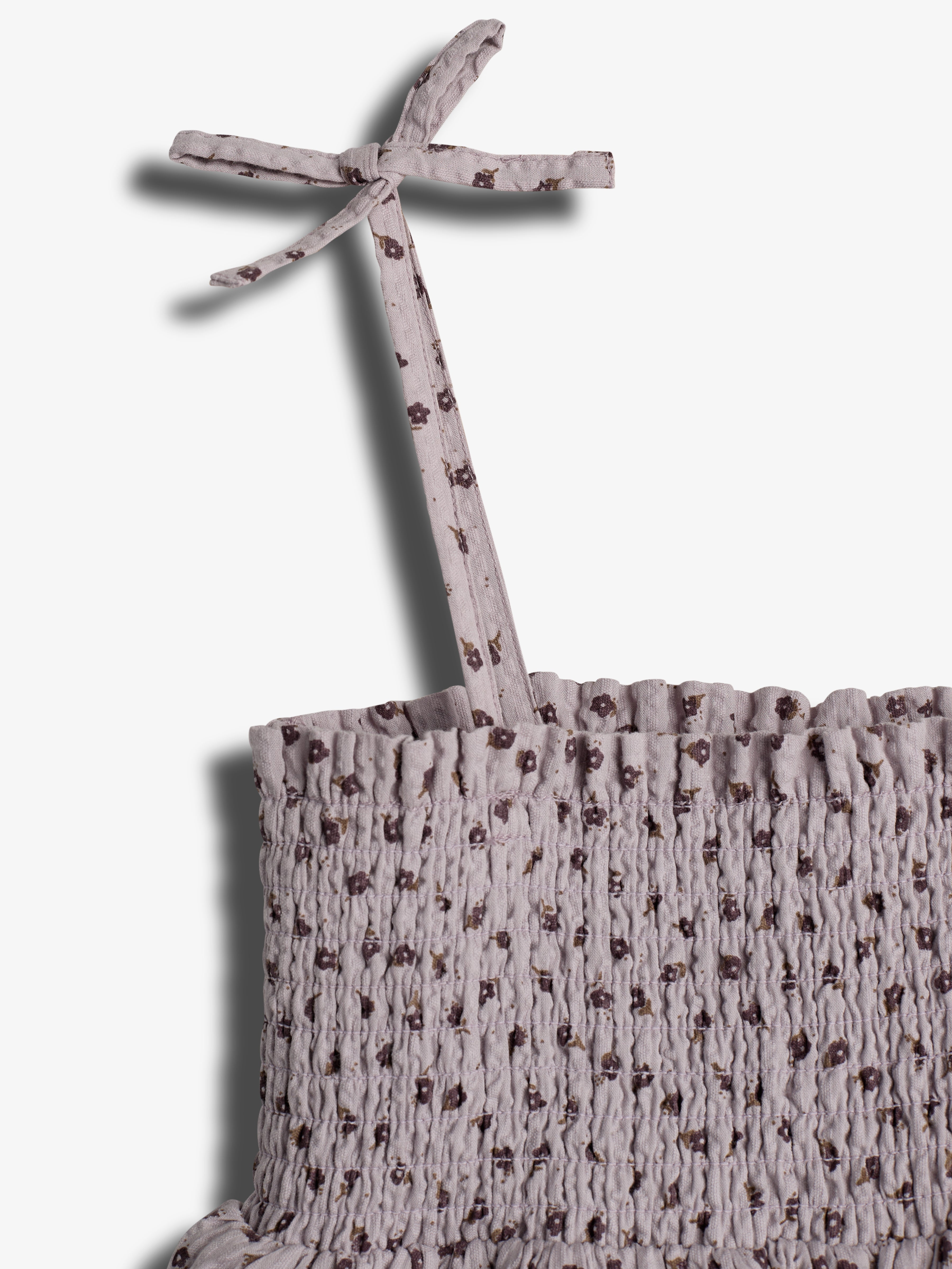 The object is a smocked fabric piece with a floral pattern, tied in a bow, attached to a greyish purple garment, set against a plain white background.