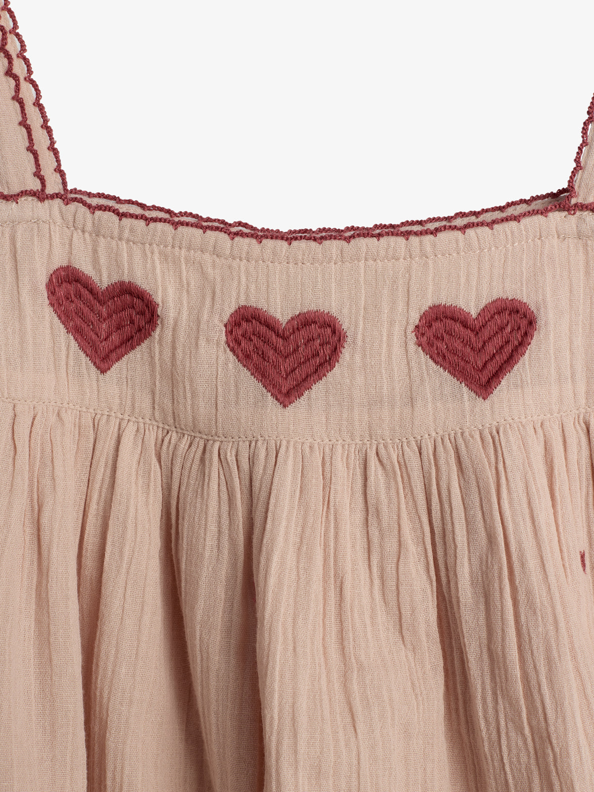 A beige fabric features three embroidered dark red hearts at the top, with scalloped edges and gathered texture below.