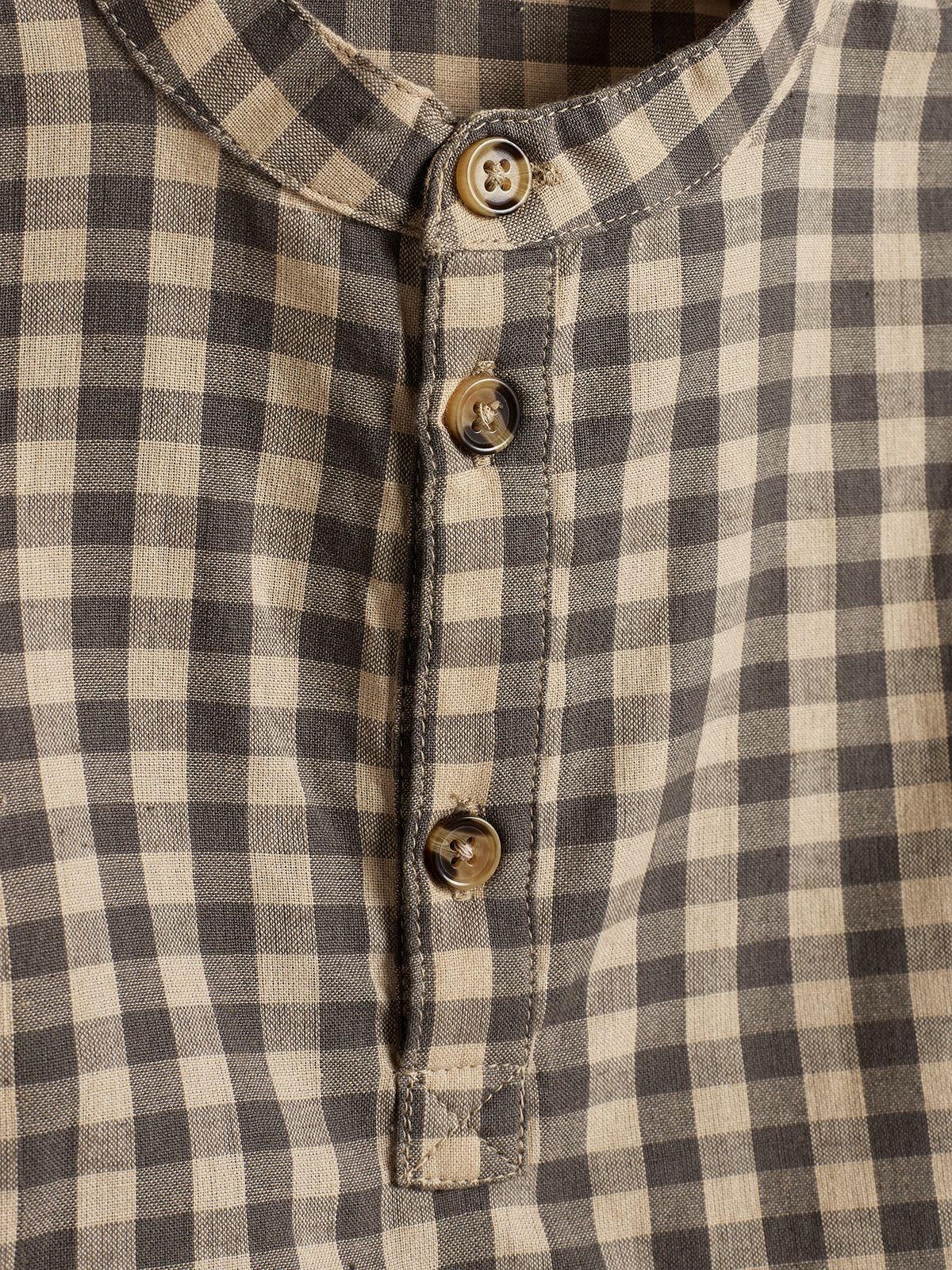 A checkered shirt featuring beige and black patterns displays three brown buttons along its placket, set against a close-up view of the fabric's textured weave.