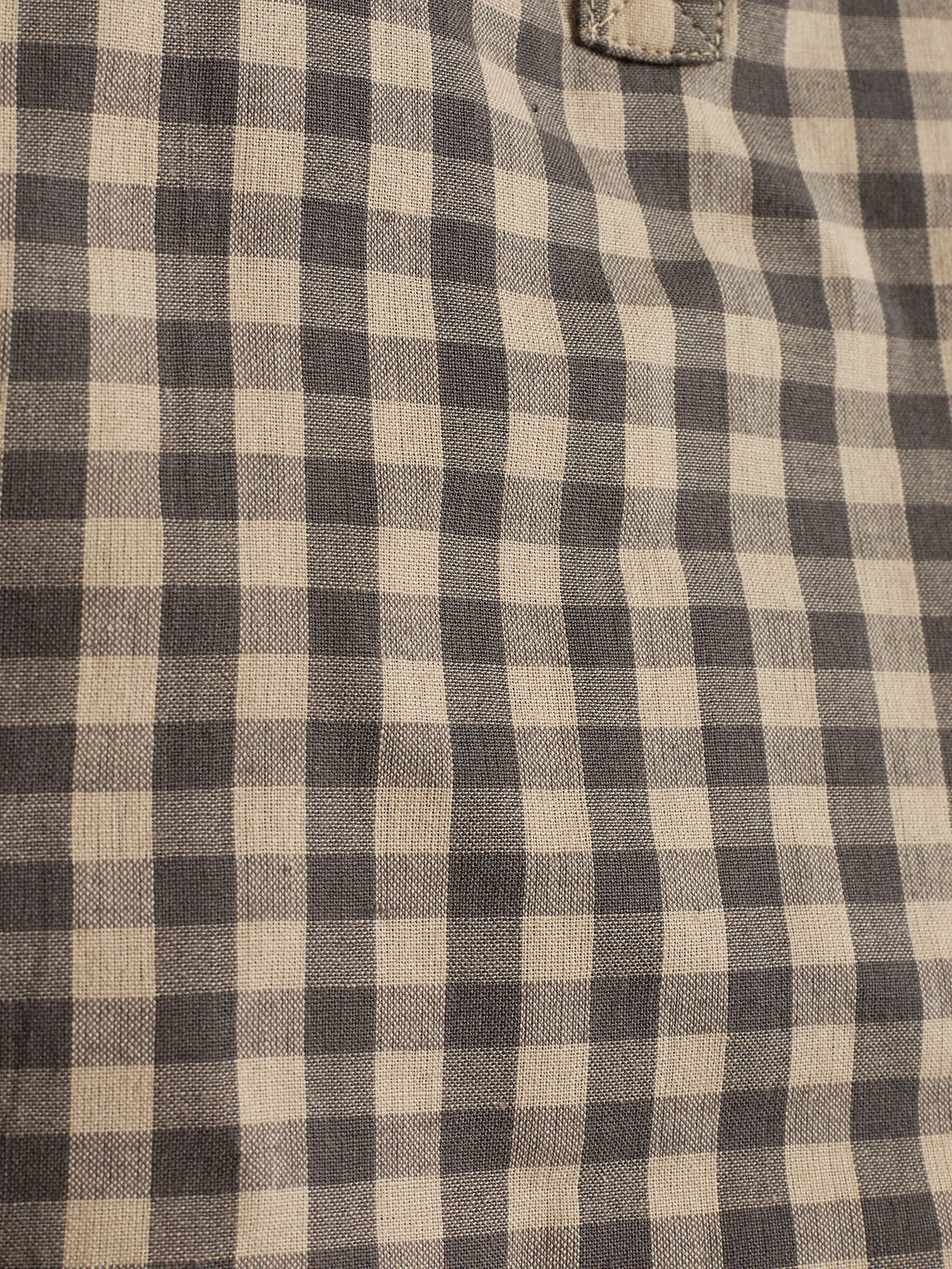 A fabric displays a black and beige gingham pattern, featuring small, evenly spaced squares. The texture appears woven, with visible stitching at the top, suggesting a garment.