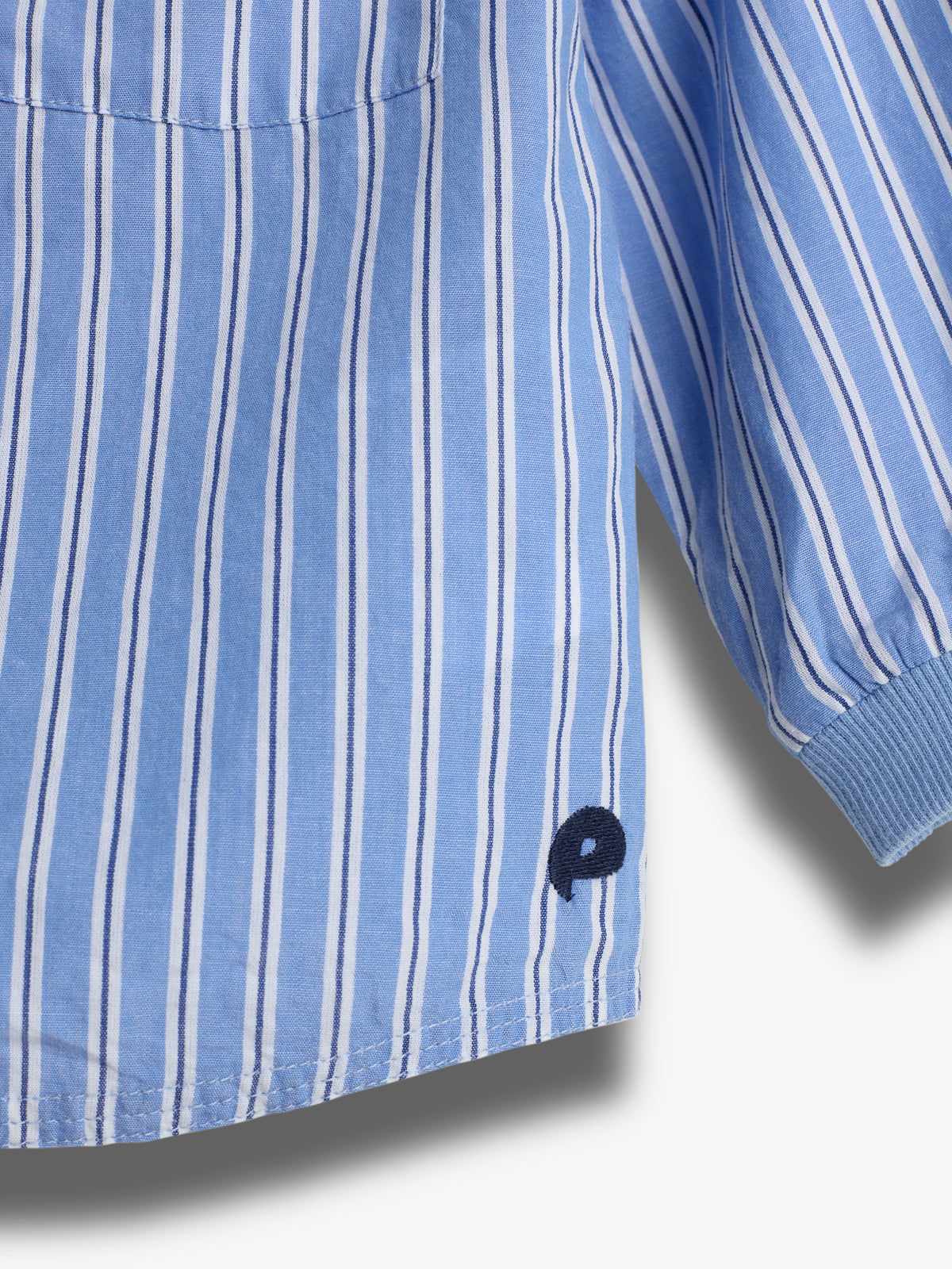 A blue and white vertically striped shirt sleeve with a ribbed cuff is shown, featuring an embroidered dark blue letter "P" near the hem.