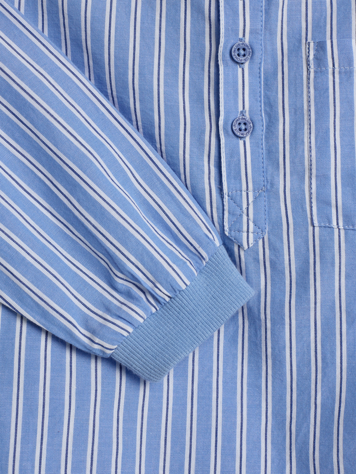 Blue striped fabric features a long-sleeve shirt with white vertical lines, ribbed cuffs, and two blue buttons near the collar, set in a casual, flat display.
