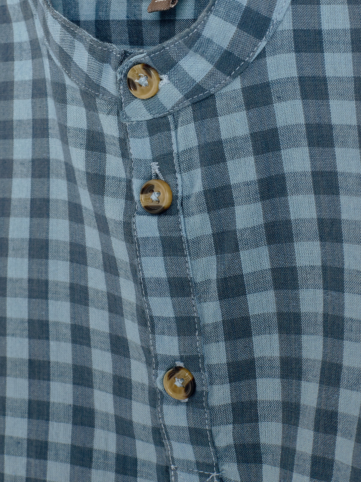 Blue and gray checkered fabric shirt with wooden buttons is showcased. The shirt is neatly buttoned and viewed up-close, emphasizing the checkered pattern and stitching details.