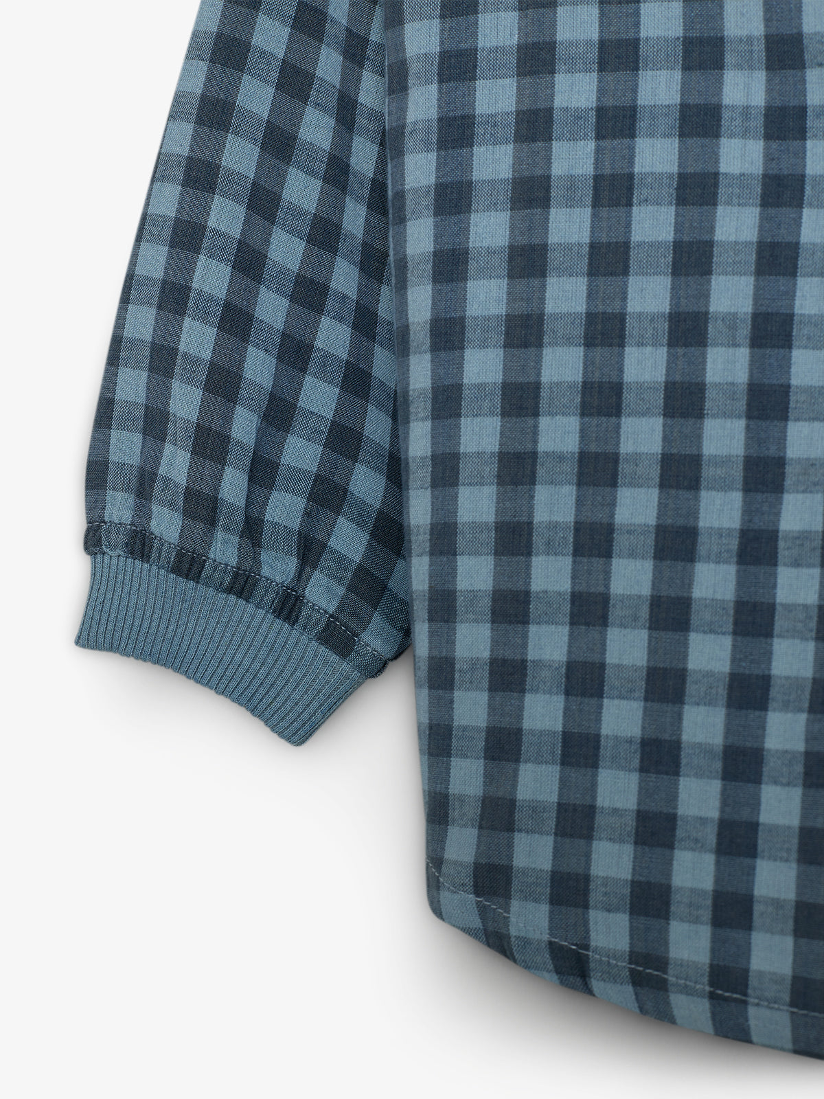 Blue and black checkered fabric forms the sleeve of a garment. The sleeve ends in a ribbed cuff, against a plain white background.