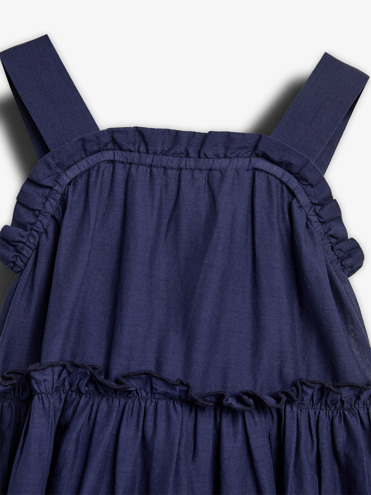 The dark blue sleeveless dress features gathered ruffles and wide shoulder straps, displayed against a plain, light background, highlighting its simple yet elegant design.