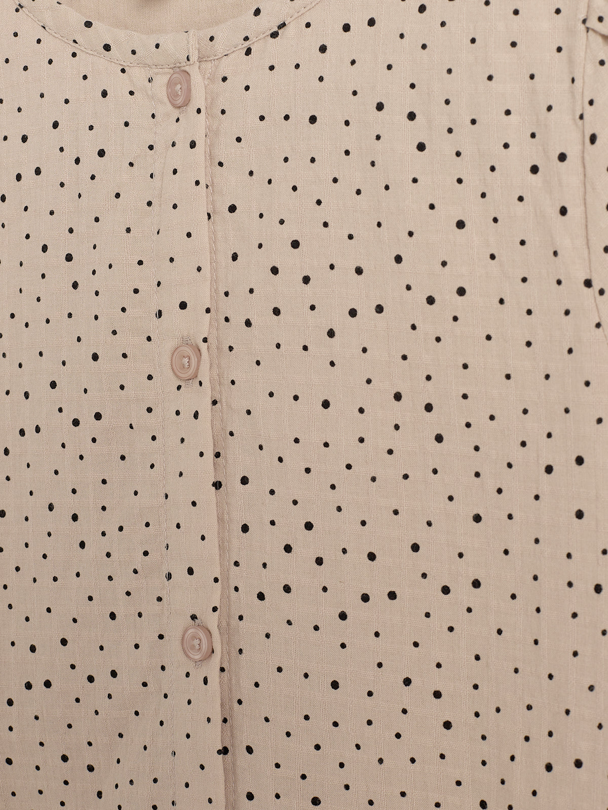 A beige fabric with a black polka dot pattern features a row of beige buttons down the center, suggesting a garment. The setting appears neutral and close-up.