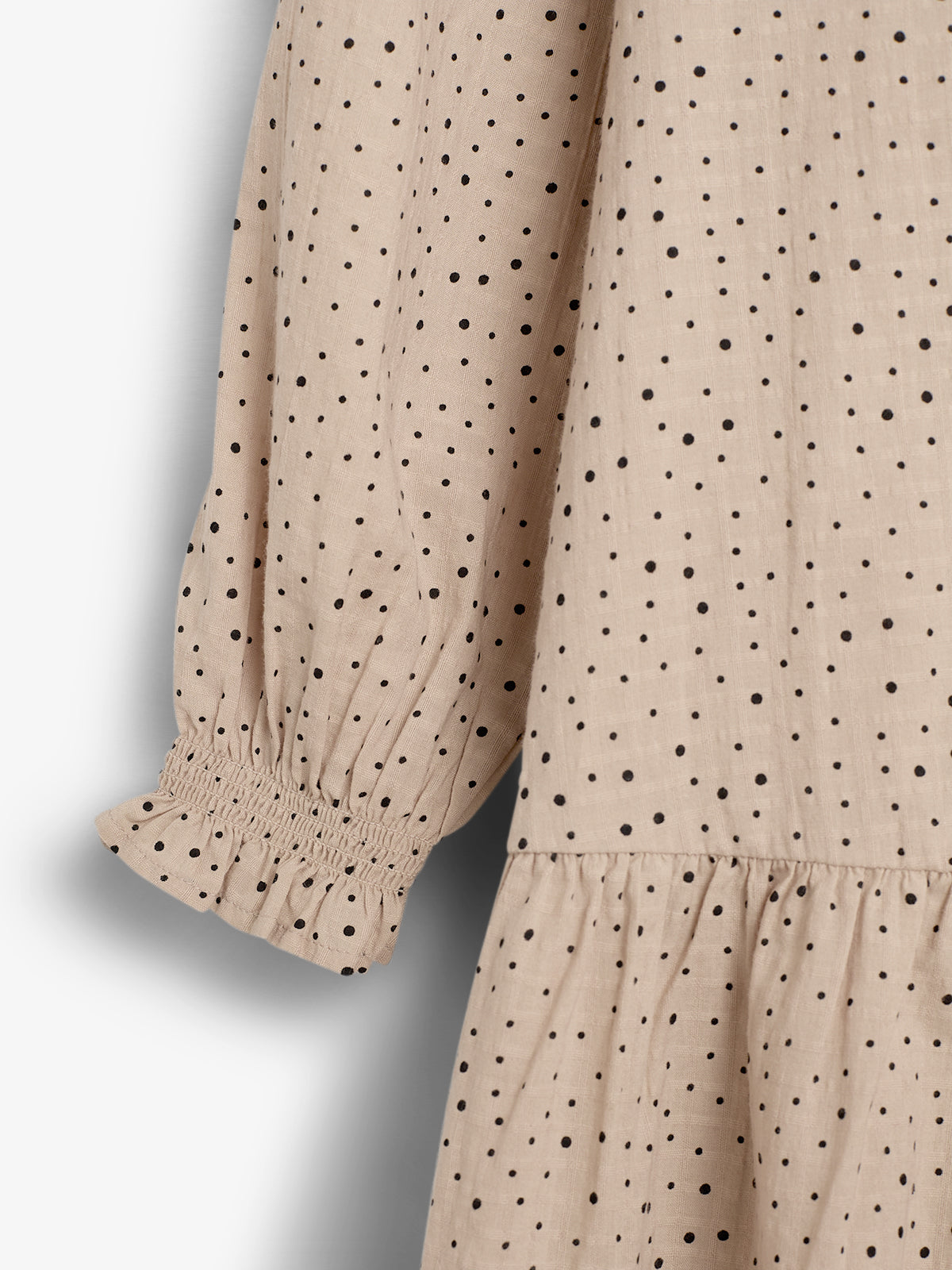 A beige fabric with black polka dots features a gathered sleeve ending in elastic cuffs, set against a plain background.