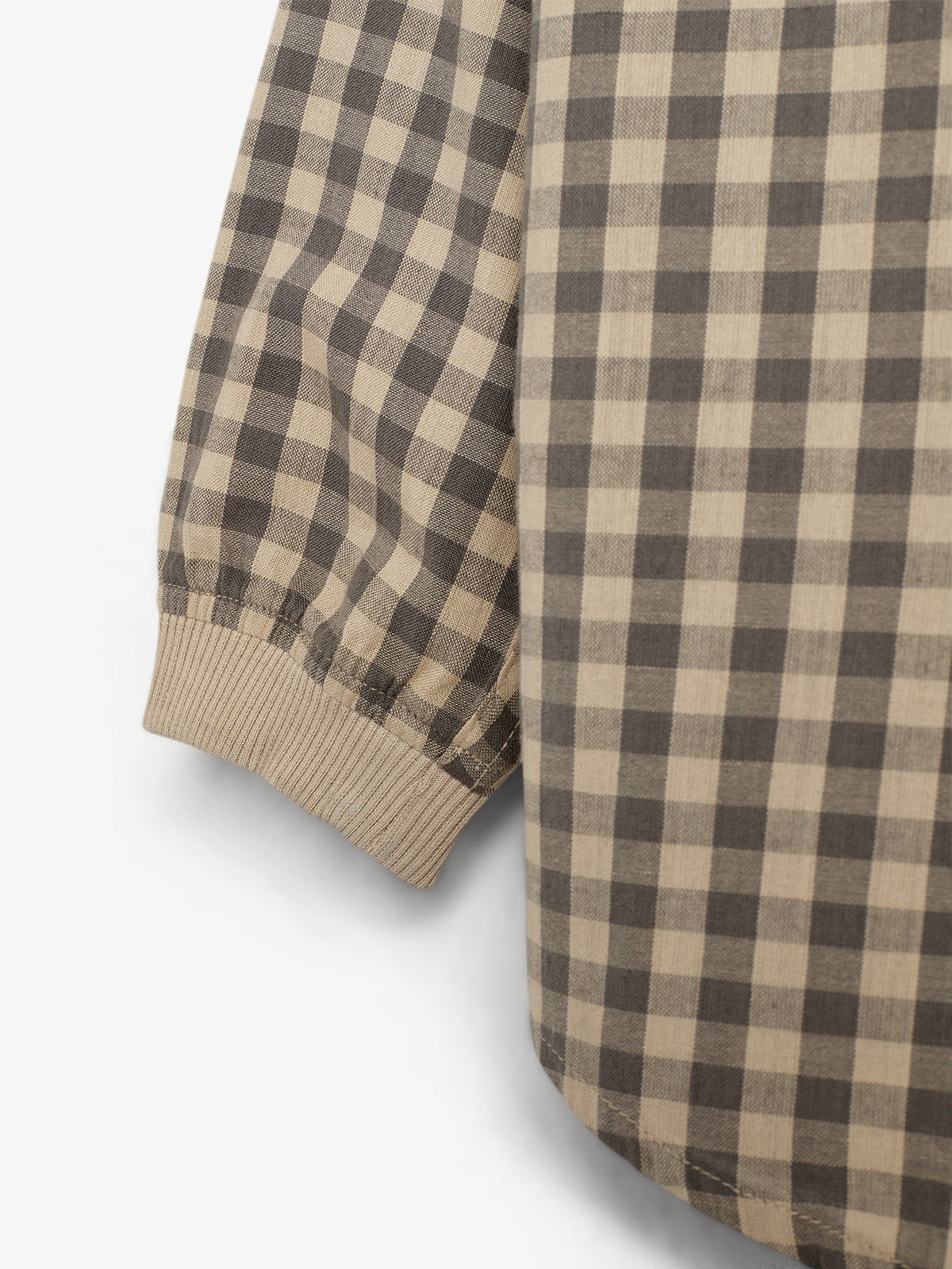 A long-sleeve shirt with a beige and brown checkered pattern shows a ribbed cuff detail, draped casually against a neutral background.