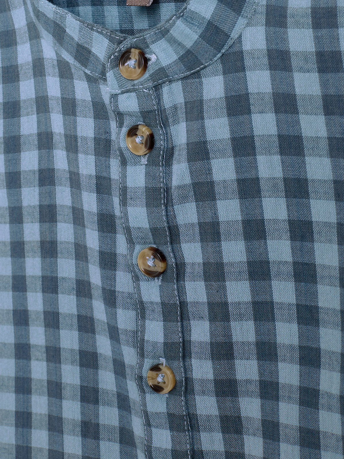 A checkered shirt with brown buttons is buttoned down. The fabric features a blue and gray pattern, and the design includes a collarless neckline, creating a casual look.