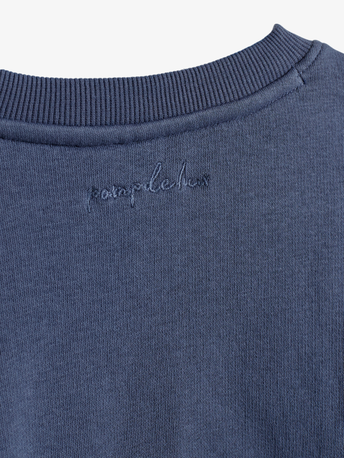 A blue ribbed neckline of a garment displays embroidered cursive text, "pamplelux," on the fabric's back. The fabric appears soft, slightly textured, and uniform in color.