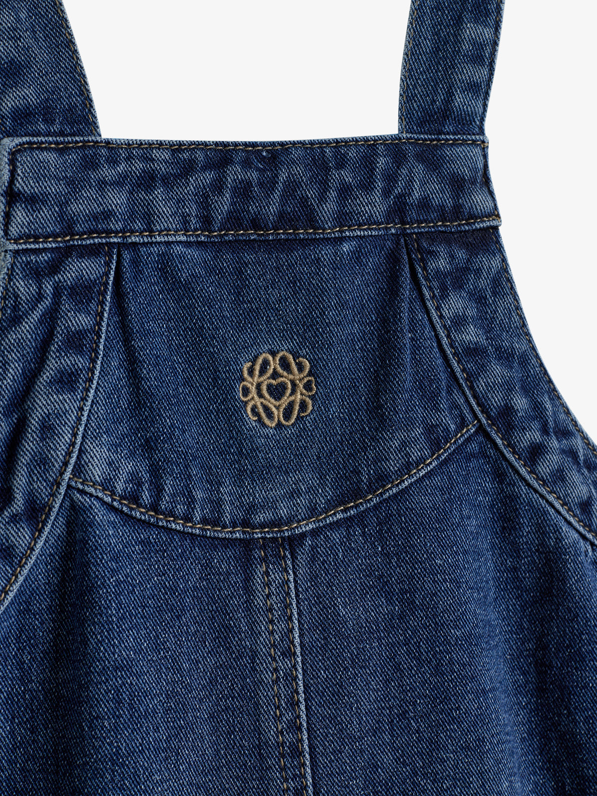 Blue denim overalls with a decorative embroidered emblem on the front. The material shows typical denim texture and stitching, framed against a plain, light-colored background.
